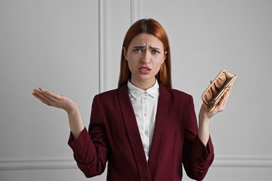 Upset woman with empty wallet near white wall