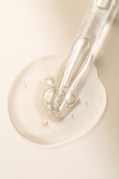 Glass pipette and transparent liquid on beige background, top view