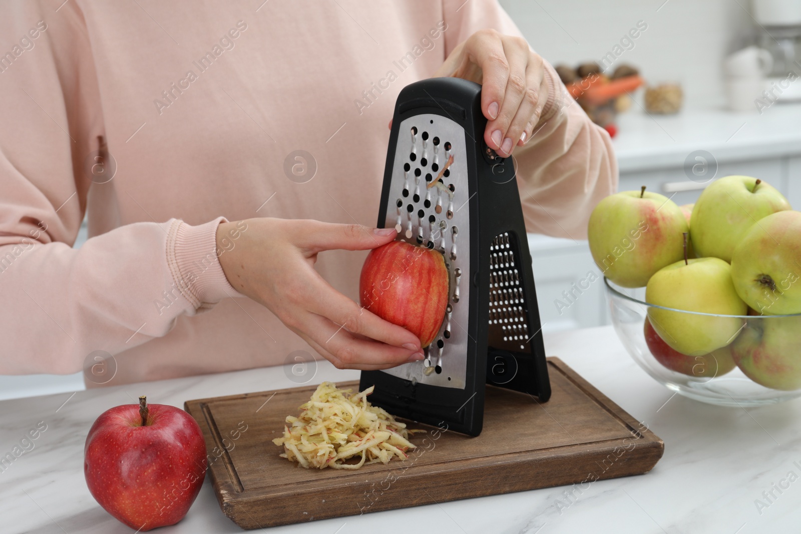 Photo of Woman grating fresh red apple at kitchen table, closeup