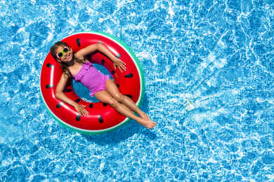 Cute little girl with inflatable ring in swimming pool, top view. Space for text 