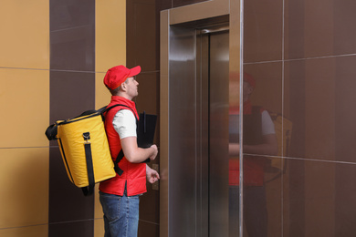 Photo of Male courier with thermo bag and clipboard waiting for elevator. Food delivery service