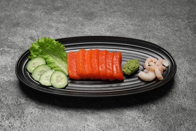 Photo of Tasty salmon slices, shrimp, cucumber and lettuce on grey table, top view. Delicious sashimi dish