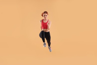Photo of Young woman in sportswear jumping on beige background