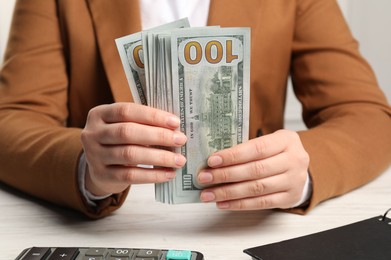 Money exchange. Woman holding dollar banknotes at white wooden table, closeup