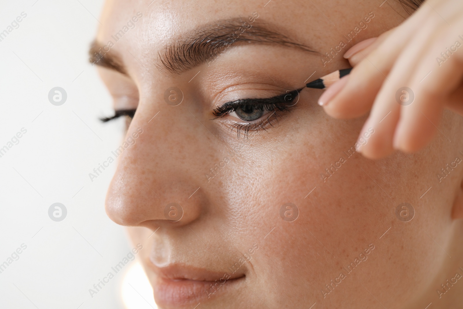 Photo of Makeup product. Woman applying black eyeliner on blurred background, closeup