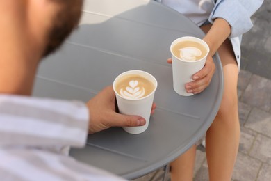 Coffee to go. Couple with paper cups at grey table outdoors, closeup