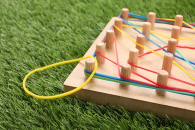 Photo of Wooden geoboard with rubber bands on artificial grass, closeup. Educational toy for motor skills development