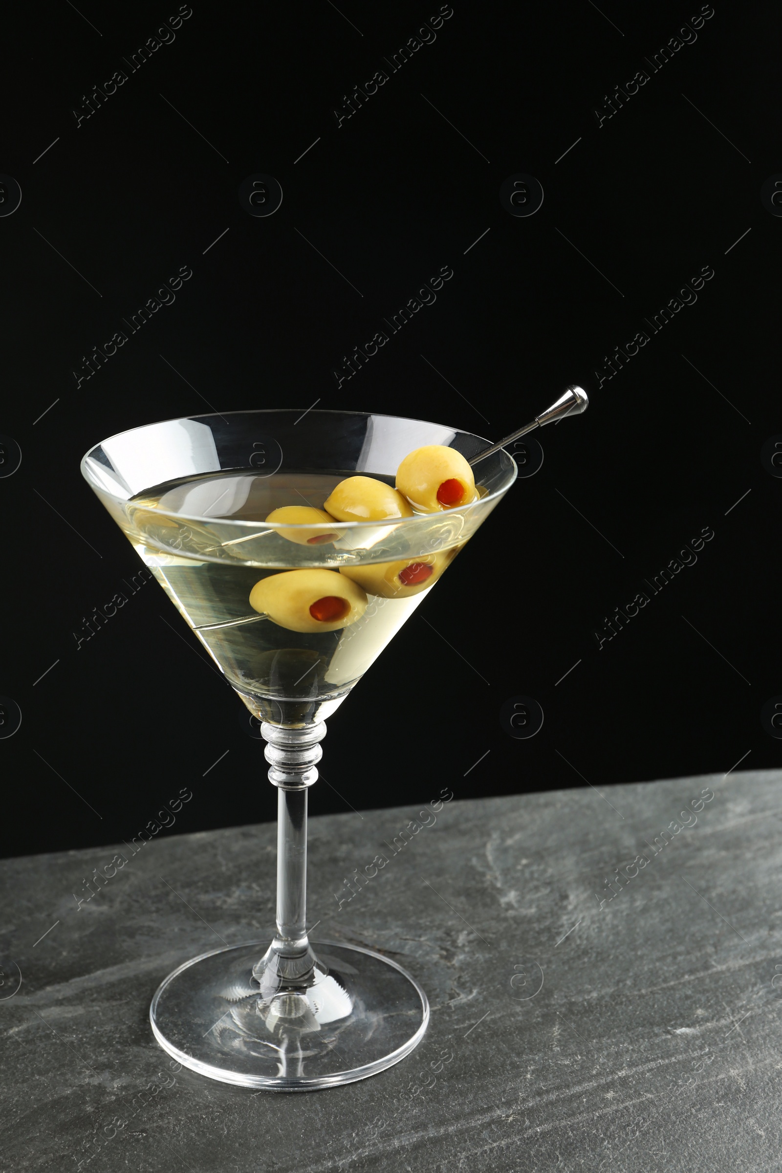 Photo of Martini cocktail with olives on grey table against dark background