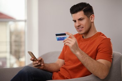 Man using smartphone and credit card for online payment on sofa at home
