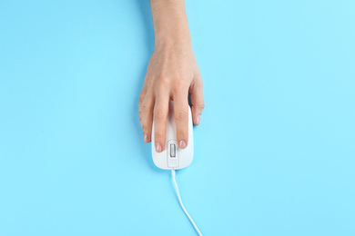 Photo of Woman using modern wired optical mouse on light blue background, top view