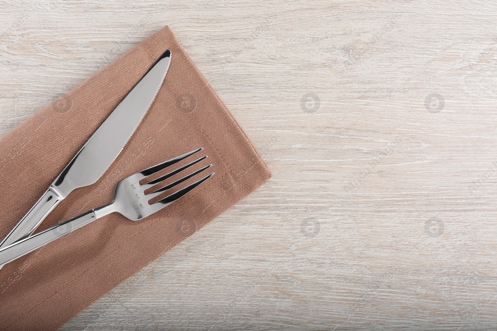 Photo of Shiny fork, knife and napkin on white wooden table, flat lay. Space for text