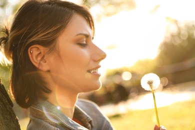 Young woman with dandelion in park on sunny day. Allergy free concept