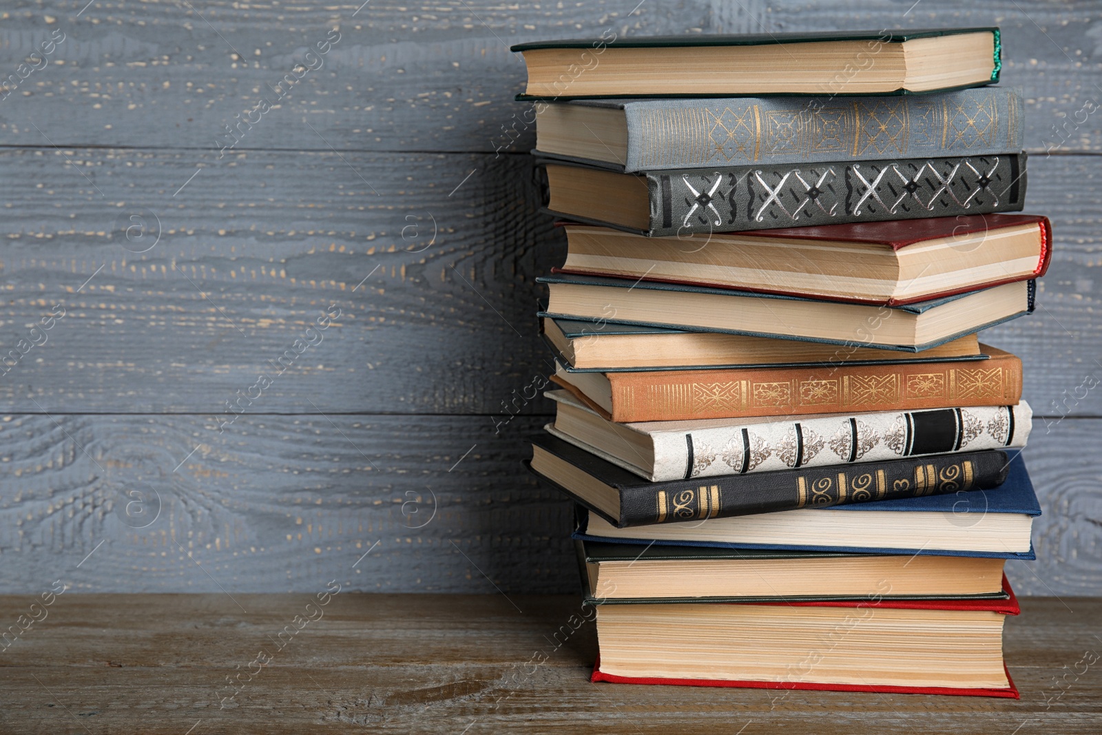 Photo of Stack of hardcover books on wooden table against grey background. Space for text