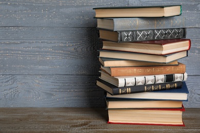 Stack of hardcover books on wooden table against grey background. Space for text