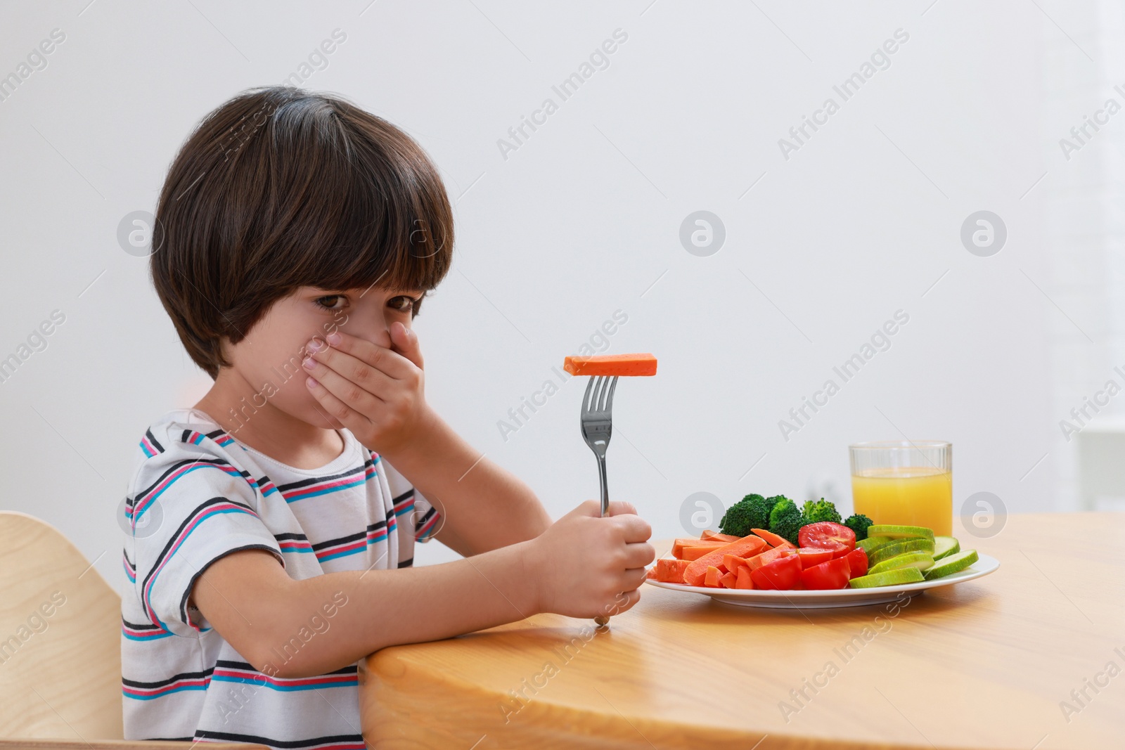 Photo of Cute little boy covering mouth and refusing to eat vegetables at home