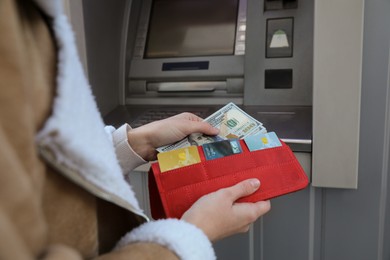 Photo of Woman putting money into wallet near cash machine outdoors, closeup