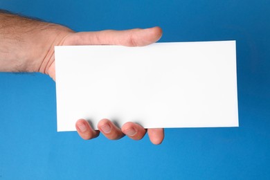 Photo of Man holding flyer on blue background, closeup. Mockup for design