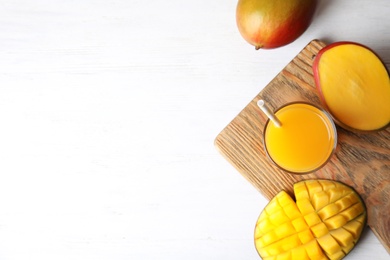 Glass of fresh mango juice and tasty fruits on wooden table, flat lay. Space for text