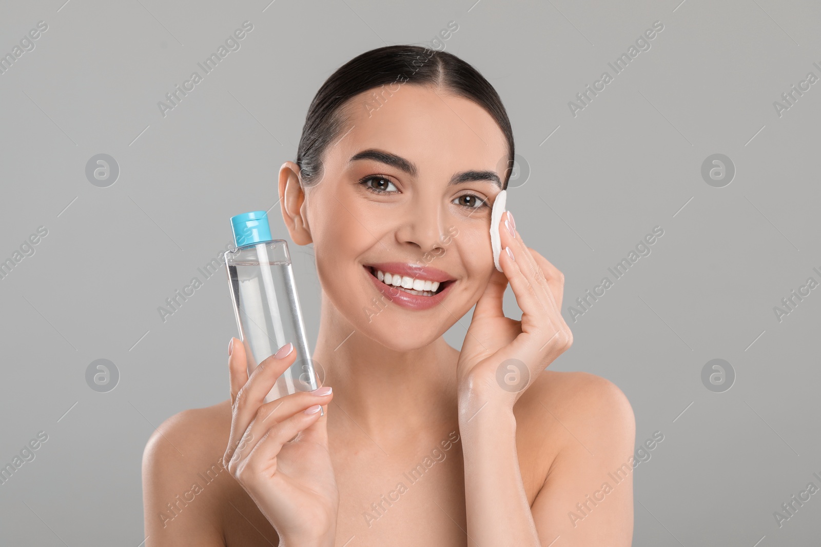 Photo of Beautiful woman removing makeup with cotton pad on light grey background