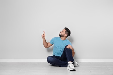Photo of Young man sitting on floor near light grey wall indoors