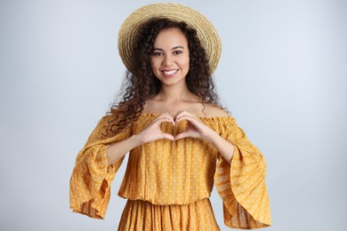 Photo of Happy young African-American woman making heart with hands on light grey background