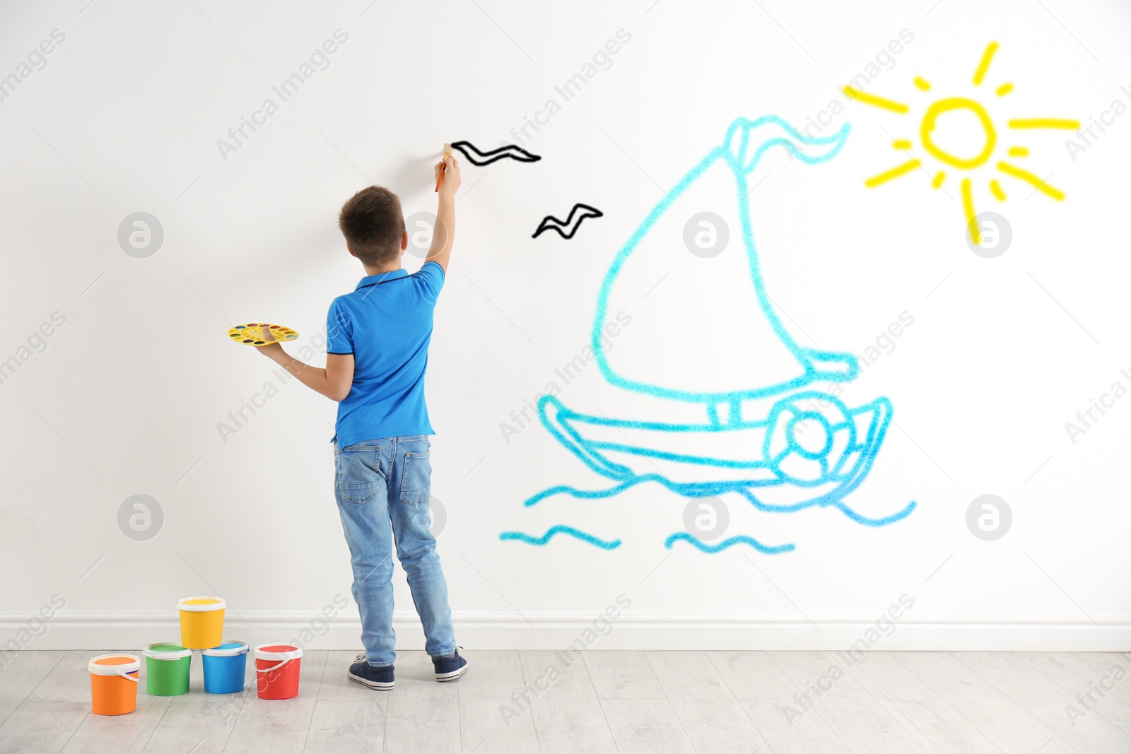 Image of Little child drawing boat at sea on white wall indoors