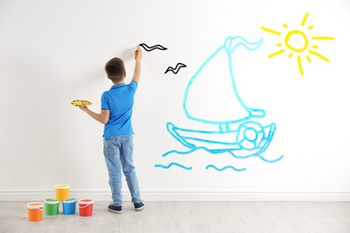 Little child drawing boat at sea on white wall indoors