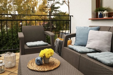 Different colorful pillows and yellow chrysanthemum flowers on rattan garden furniture outdoors