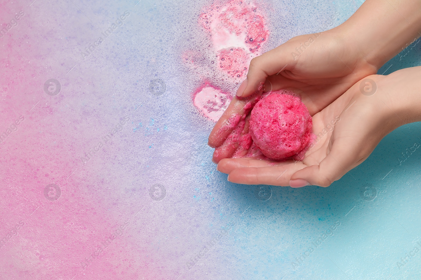 Photo of Woman holding bath bomb over water with foam, top view. Space for text