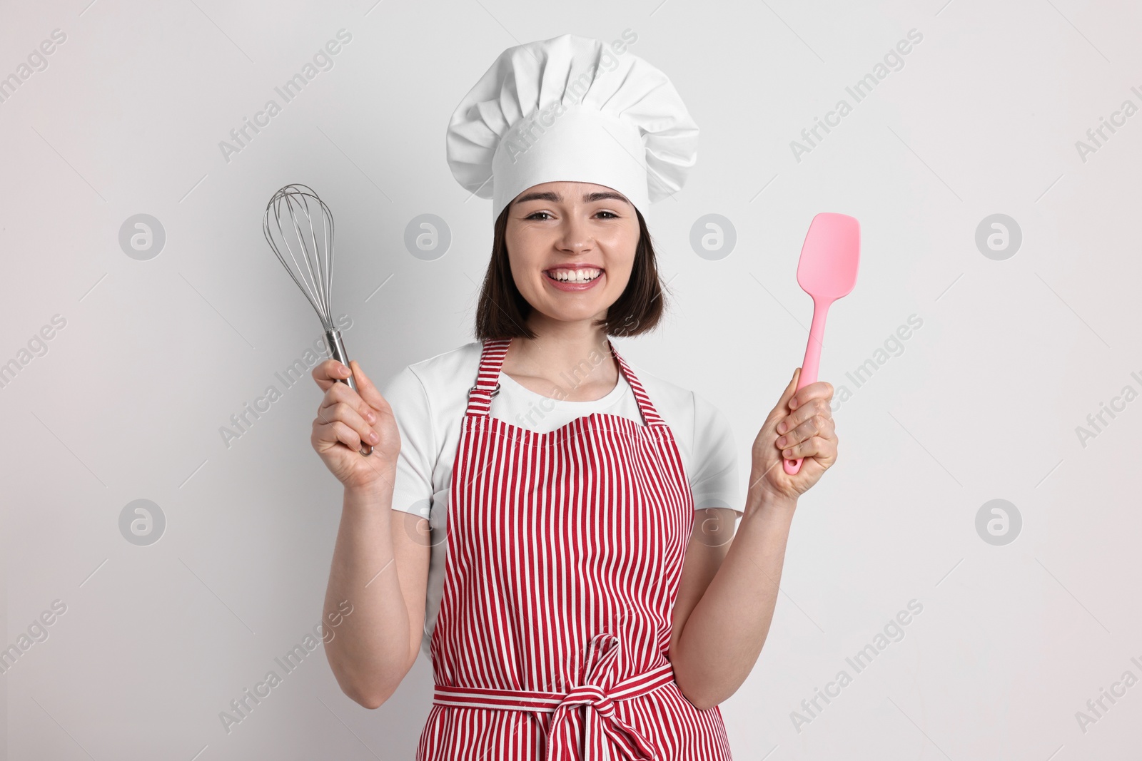 Photo of Happy confectioner holding whisk and spatula on light grey background