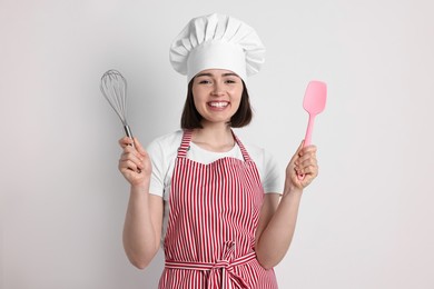 Happy confectioner holding whisk and spatula on light grey background