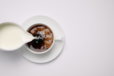 Pouring milk into cup of coffee on white background, top view