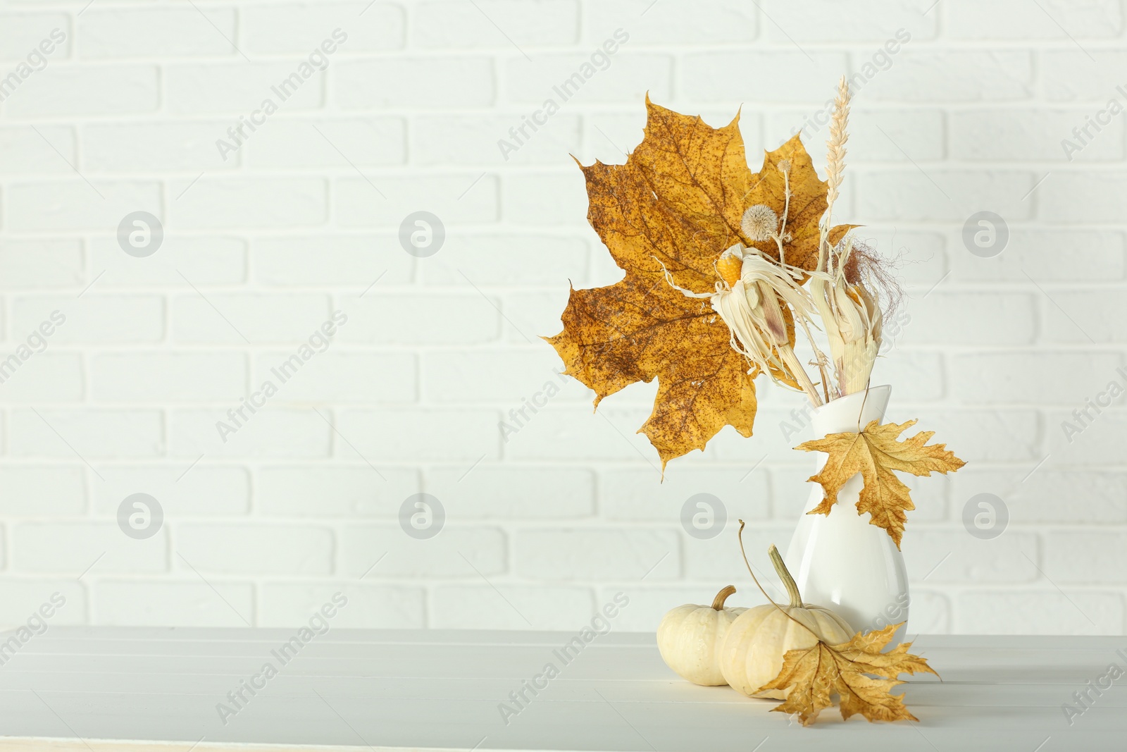 Photo of Composition with beautiful autumn leaves and pumpkins on table against white brick wall, space for text