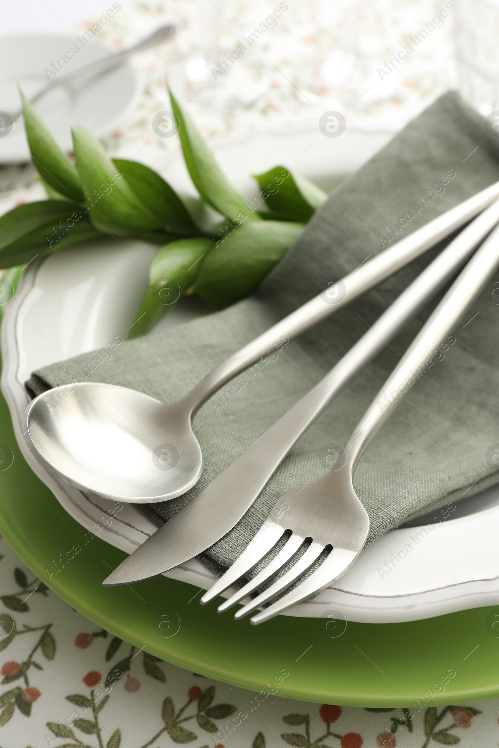 Photo of Stylish setting with cutlery, plates, napkin and floral decor on table, closeup