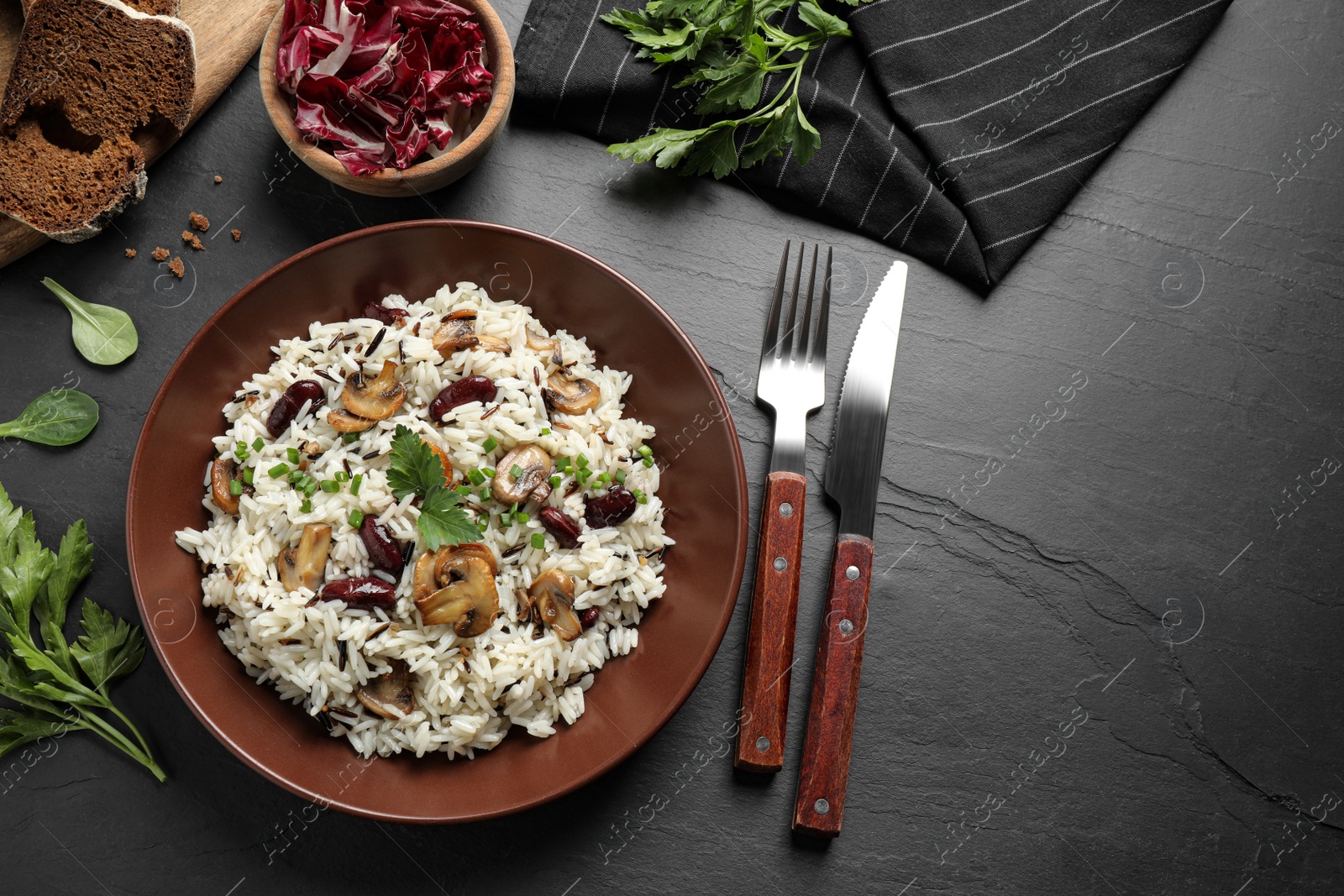 Photo of Delicious rice pilaf with mushrooms served on black table, flat lay