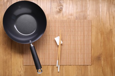 Empty iron wok and chopsticks on wooden table, top view. Space for text