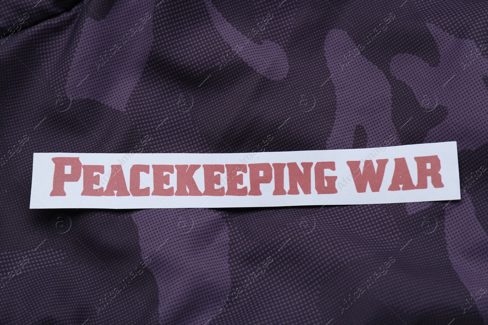 Photo of Paper card with phrase Peacekeeping War on color fabric, top view