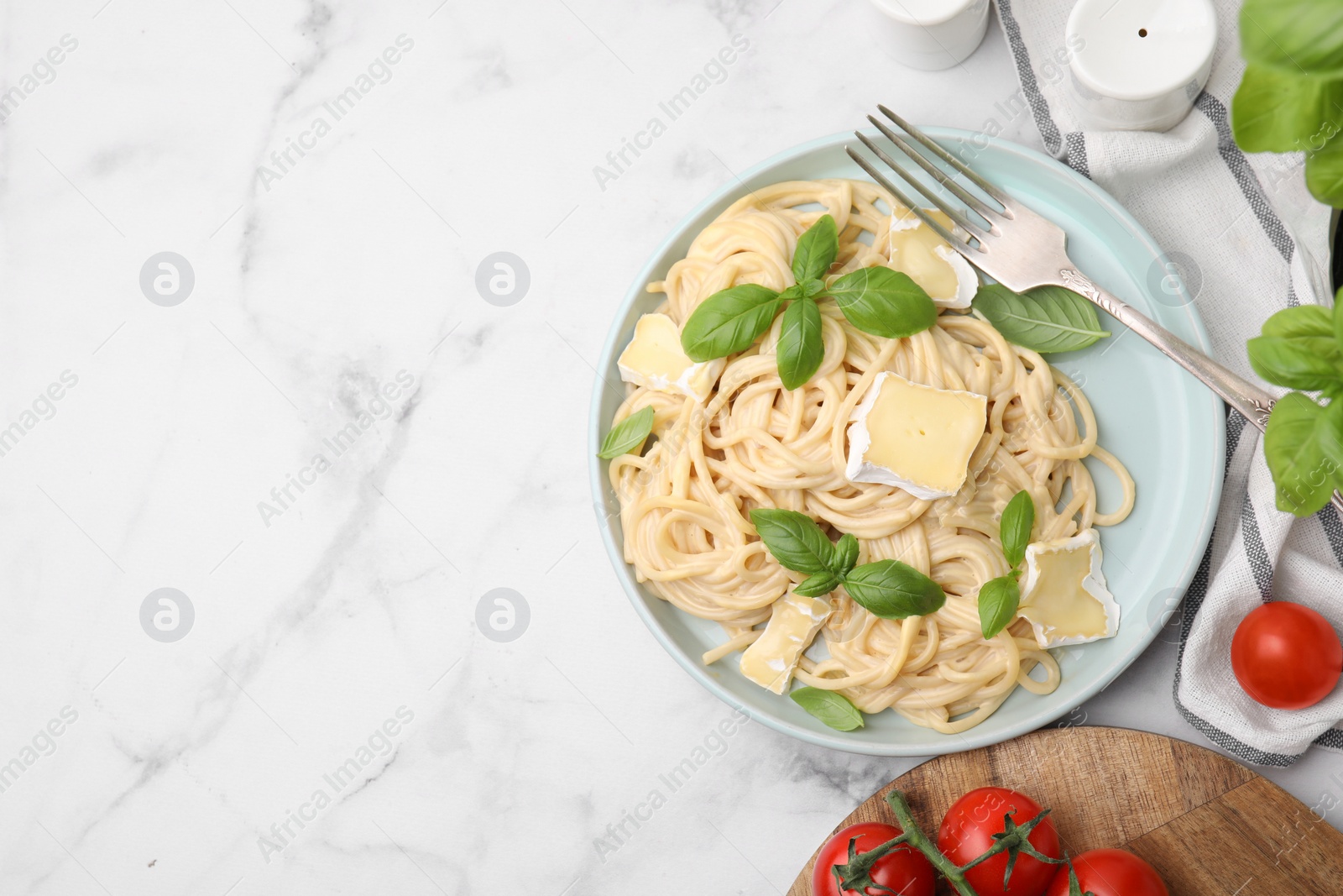 Photo of Delicious pasta with brie cheese, basil and fork on white marble table, flat lay. Space for text