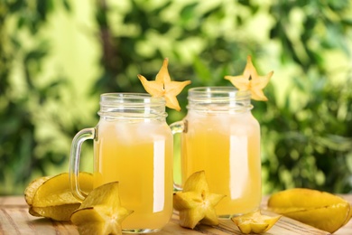 Photo of Delicious carambola juice and fresh fruits on wooden board against blurred background, closeup