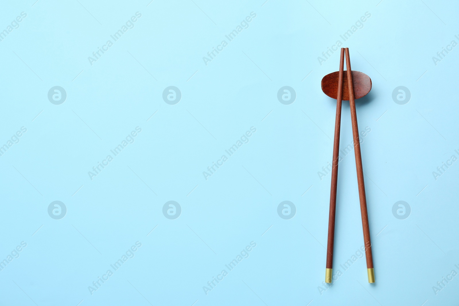 Photo of Pair of wooden chopsticks and rest on light blue background, top view. Space for text