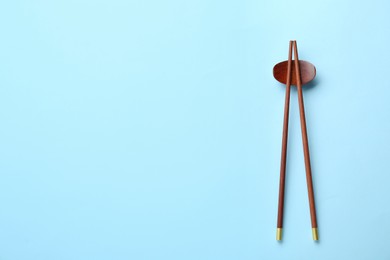 Pair of wooden chopsticks and rest on light blue background, top view. Space for text