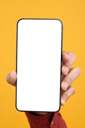 Man holding smartphone with blank screen on yellow background, closeup