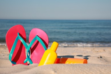 Photo of Stylish flip flops and sunscreen on beach. Space for text