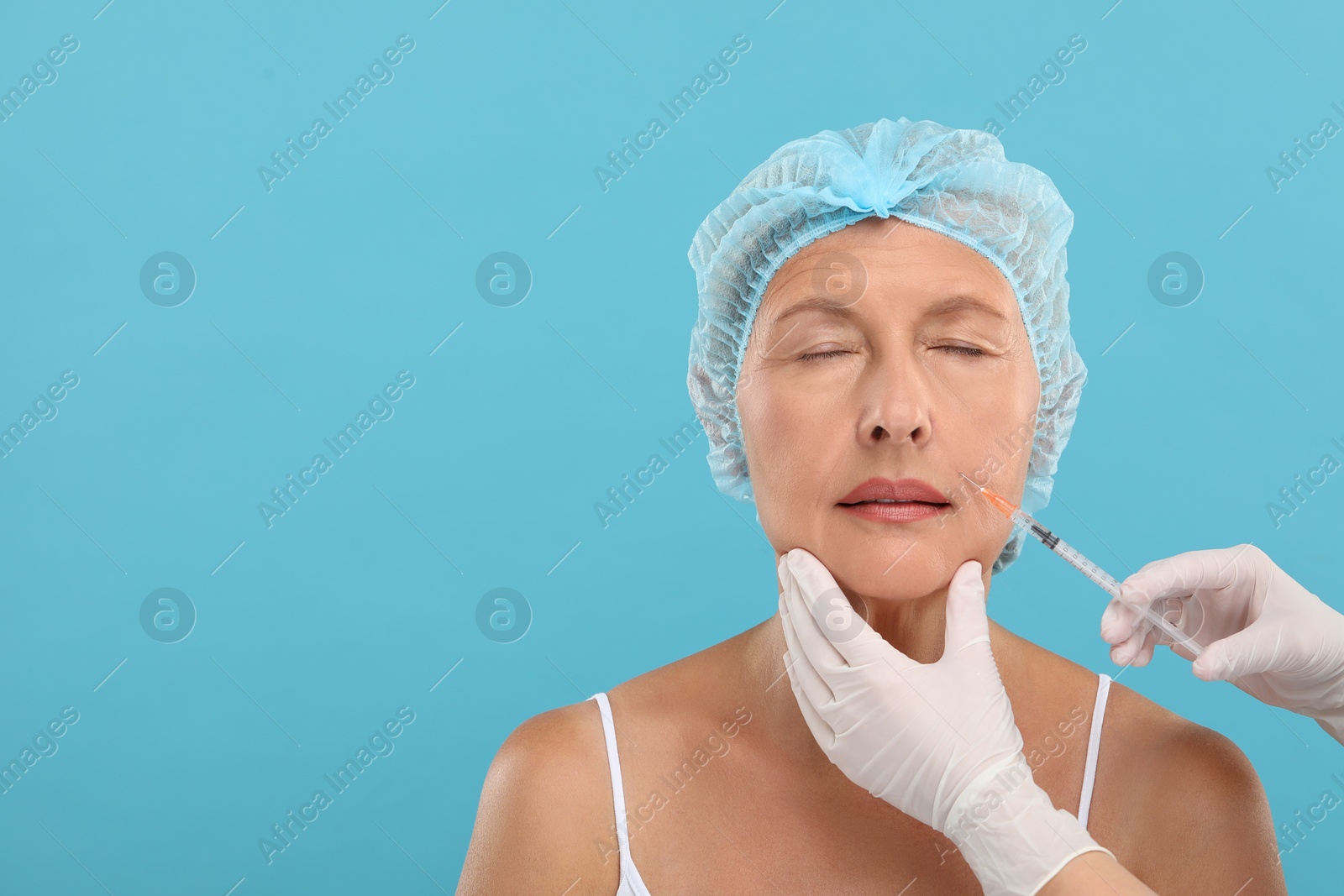 Photo of Doctor giving facial injection to senior woman on light blue background, space for text. Cosmetic surgery