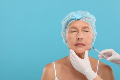 Photo of Doctor giving facial injection to senior woman on light blue background, space for text. Cosmetic surgery