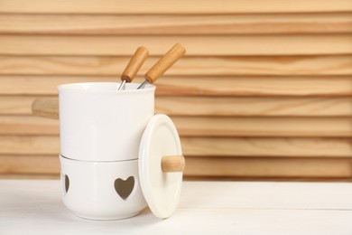 Fondue set on white wooden table, space for text