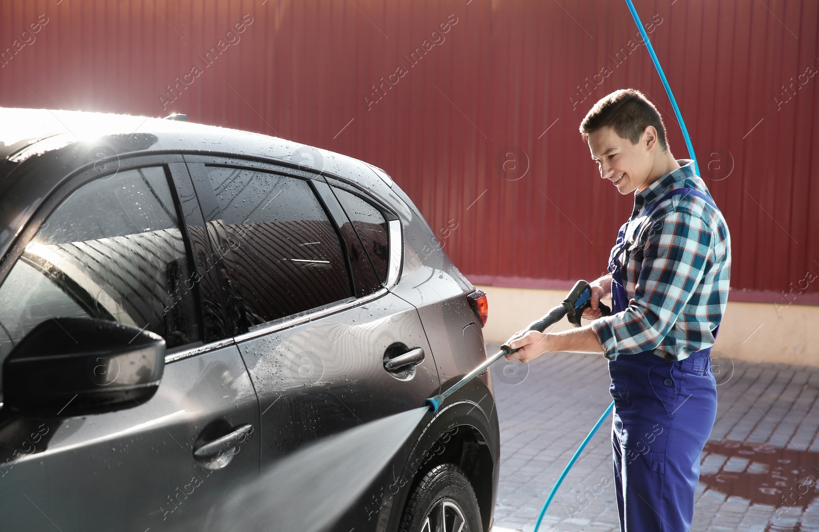 Photo of Worker cleaning automobile with high pressure water jet at car wash