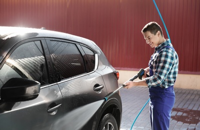 Worker cleaning automobile with high pressure water jet at car wash