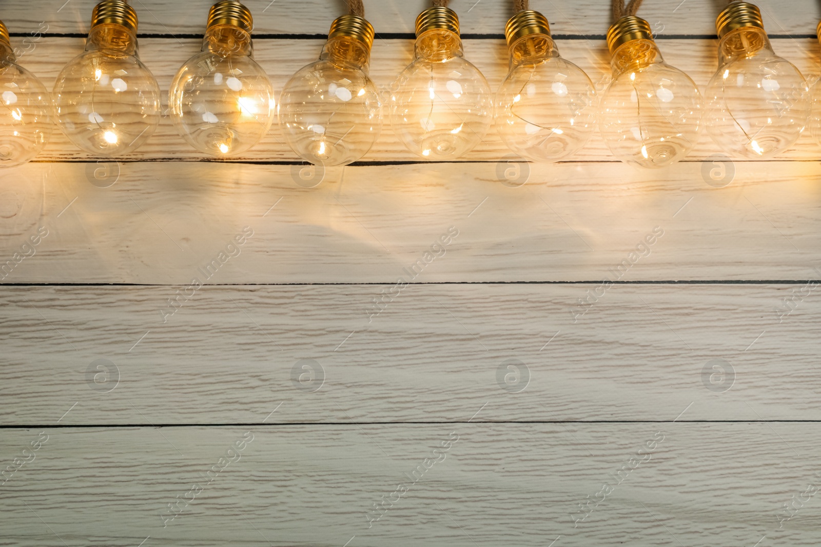 Photo of String lights with lamp bulbs on wooden background, top view. Space for text