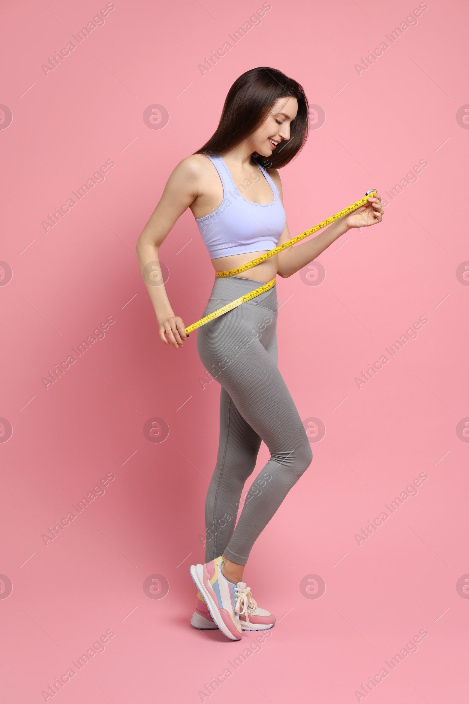 Photo of Happy young woman with measuring tape showing her slim body on pink background